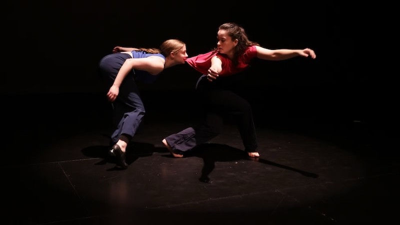 Two dancers on a dark stage - one biting the shirt of the other