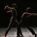 Two dancers, one with an ancient mask, perform a duet, lunging towards each other with their arms thrown back