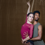 Two ballet dancers gaze past the camera in an embrace with arms extended
