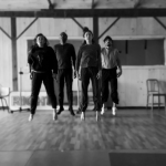 A black and white photo of four dancers in a studio leaping in the air