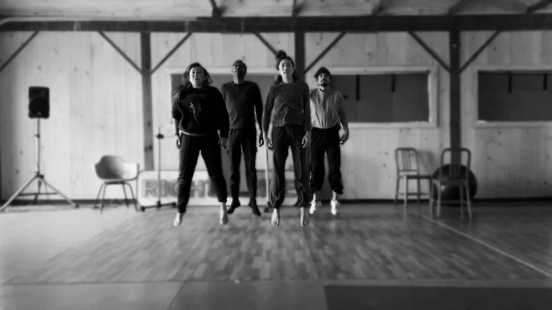 A black and white photo of four dancers in a studio leaping in the air