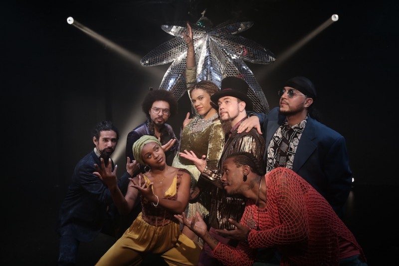 The cast of Cannabis! in colorful costumes and posing in front of a disco ball shaped like a marijuana leaf