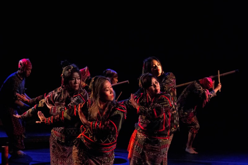 Members of Kinding Sindaw dancing in unison on stage wearing red and black patterned traditional costumes; four dancers are in t