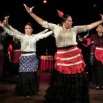 Flamenco dancers on stage with their arms raised in the air