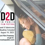 A woman in yellow and blue glances against a half open paint glass window 