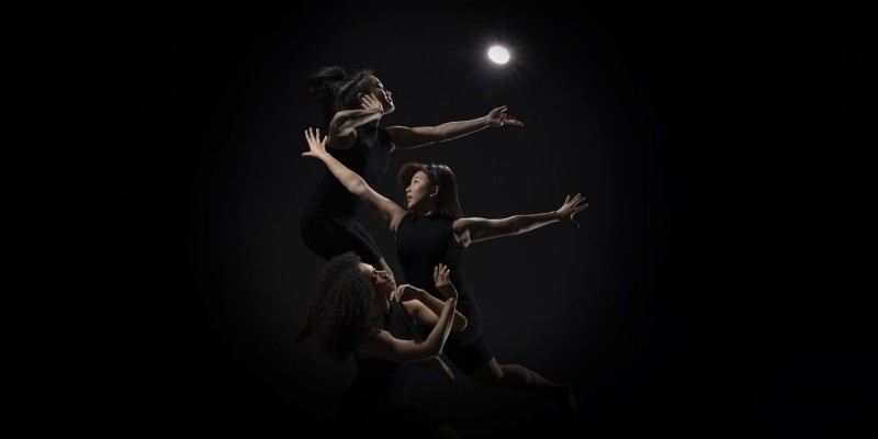 3 dancers in a row from top to bottom appear backlit from a single streetlamp