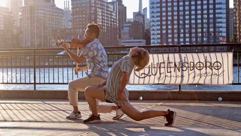 Waterfront show, male dancer playing a violin next to female dancer in backbend