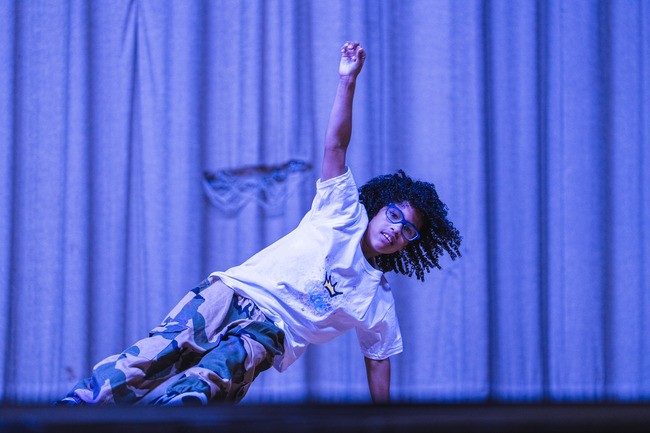 young dark skinned dance student with natural curly hair doing a breakdance move on stage