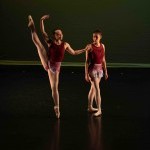 Two dancers on stage, one with leg lifted, the other making a funny face