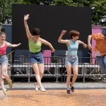 Four people dancing and jumping on a wooden stage