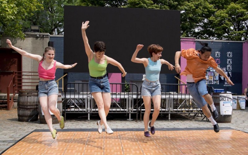 Four people dancing and jumping on a wooden stage