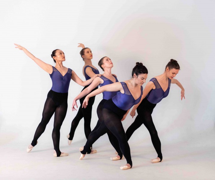 Five dancers in pointe shoes together posing like a giant bird