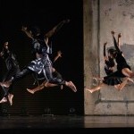 Dancers on stage jumping, with exposed brick wall