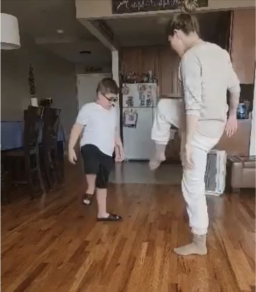A teacher and student both lifting one leg up off the ground and looking at their feet. 