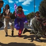 A colorful photo of a group of dancers mid-motion on a basketball court. 