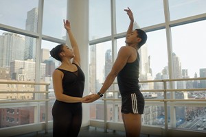 Two dances face each other holding hands while they extend their other arm the ceiling