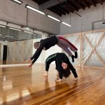 One dancer jumping over another dancer in a studio