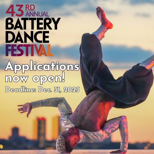 A break dancer does a shoulder stand in front of a sunset sky.