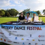 Three women sit at a table in an outdoor park selling Battery Dance merchandise