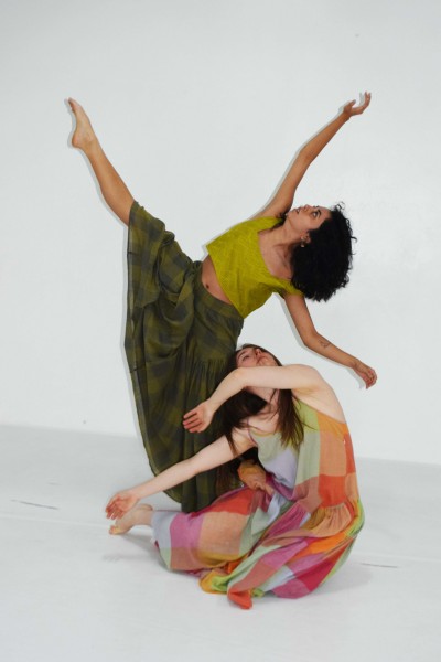 Two dancers in colorful dress, one dancer with leg and arms stretched out and the other seated on the ground