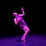 Rush, a white dancer in a purple dress, stands in a leaned back pose in purple lighting
