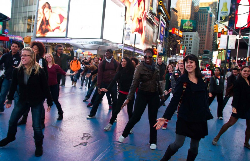 a diagonal line of dancers extend their hands to the ground. Wintertime in Times Square