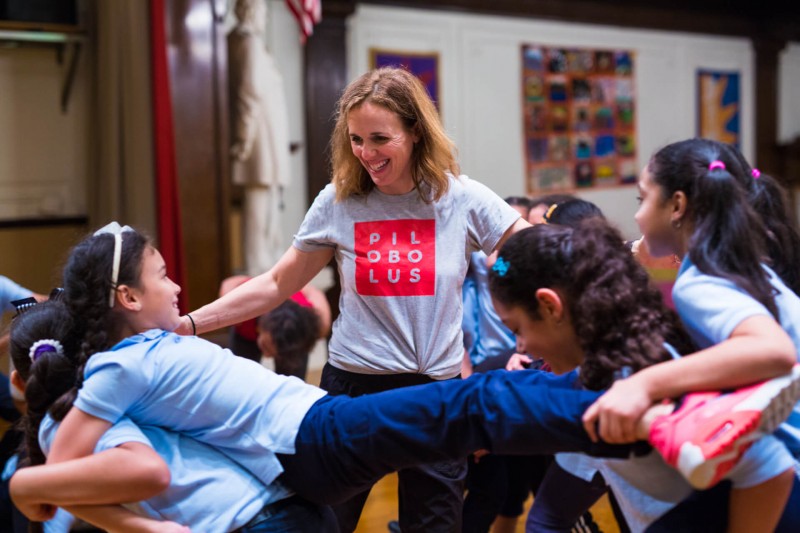 Teaching Artist with arms outstretched towards two young dancers in a backbend lift.