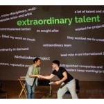 two performers in front of a projection of words 