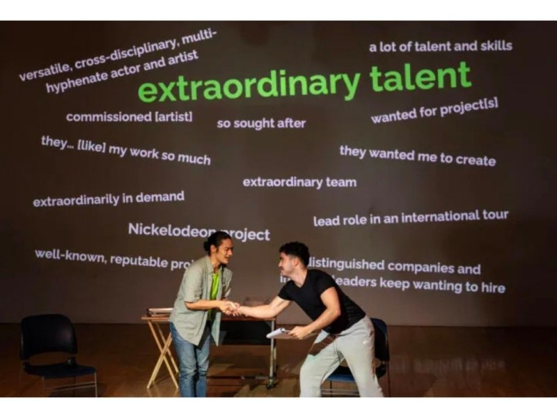 two performers in front of a projection of words 