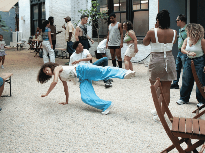 ID: People gathered in open courtyard. Dancer is in motion at a low level with a leg and an arm in the air.