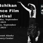 Black & white photo, one dancer stands with her back towards camera arms swaying to left, a second dancer sits in front