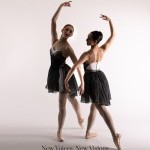 Two dancers pose in pointe shoes, arms are intertwined.