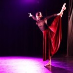 Dancer holding her left leg out to the side, wearing a black leotard and black long skirt.