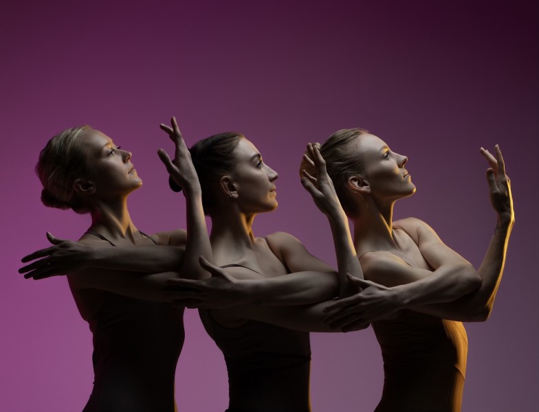 Three dancers facing right, one behind the other, with their arms raised and intertwined 