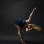 cis white female bending body forward with hair flip. Shes a navy satin dress.