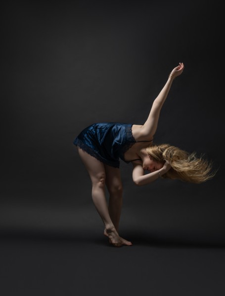 cis white female bending body forward with hair flip. Shes a navy satin dress.