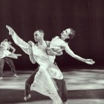 One dancer supporting another, leg up high to the side.