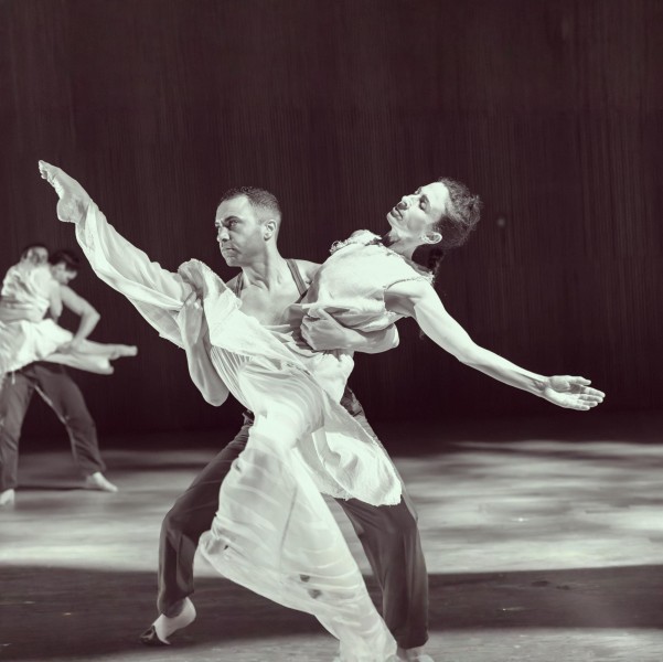 One dancer supporting another, leg up high to the side.