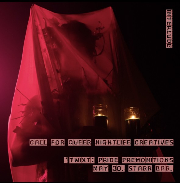 A performed in a red veil holds two candles. They are dressed in elaborate, forest themed drag amidst a dark background. 