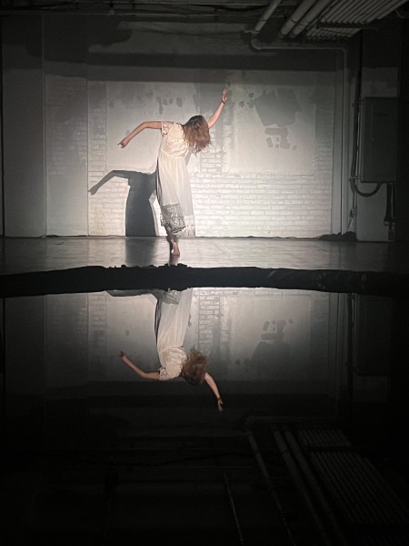Dancer in old white dress is reflected in a black lake in an abandoned warehouse