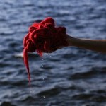 red yarn sculpture held by a hand in front of a body of water