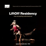 A performer sits on the floor against a dark background. She wears grey pants and a pink piñata on her head obscuring her face.