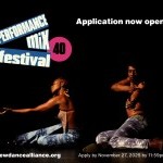 Two dancers sit on the floor against a dark background. One dancer reaches forward, the other reaches towards the camera.