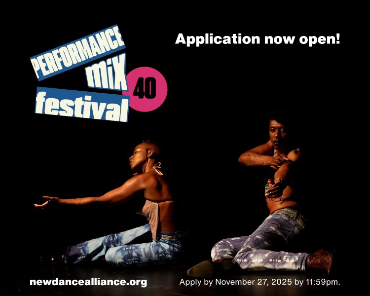 Two dancers sit on the floor against a dark background. One dancer reaches forward, the other reaches towards the camera.