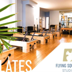 Pilates reformers lined up with Flying Squirrel Studios logo on the bottom right corner and greenery on the left side of the pic