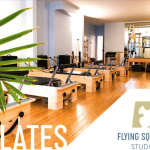 Pilates reformers lined up with Flying Squirrel Studios logo on the bottom right corner and greenery on the left side of the pic