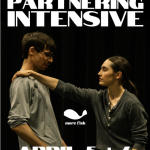 A dancer with long brown hair tied back in a ponytail holds the shoulder of a dancer with short brown hair.