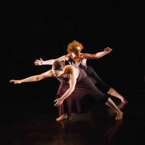 Two dancers reach out with straight arms as though searching