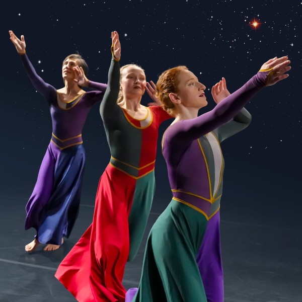 Three dancers in jewel-tone dresses stride forward with one arm outstretched and one hand cupped at their mouths