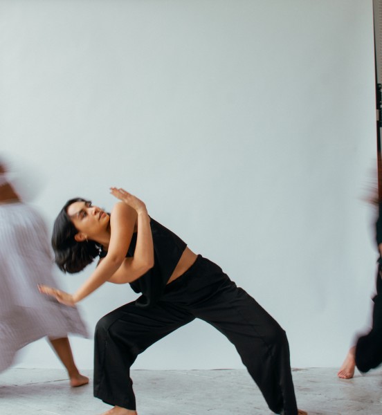Unbound Dance Collective company member Sara Long poses in a black outfit with blurred figures in motion in the background